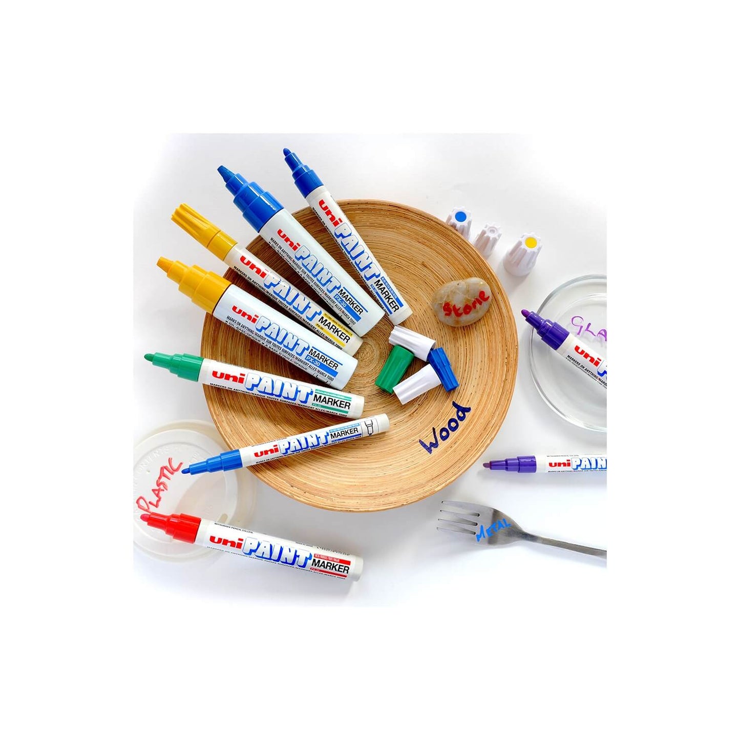uni-ball paint markers on a white surface with a wooden plate and fork.