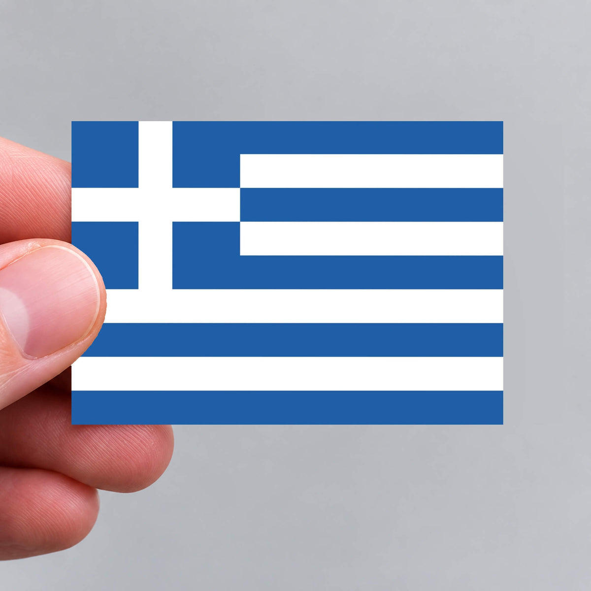 A hand holding a Greek flag sticker