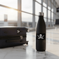 Black water bottle and suitcase with jolly roger stickers in an airport setting