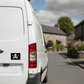 White van with a jolly roger / pirate flag sticker on the back, driving down a street.