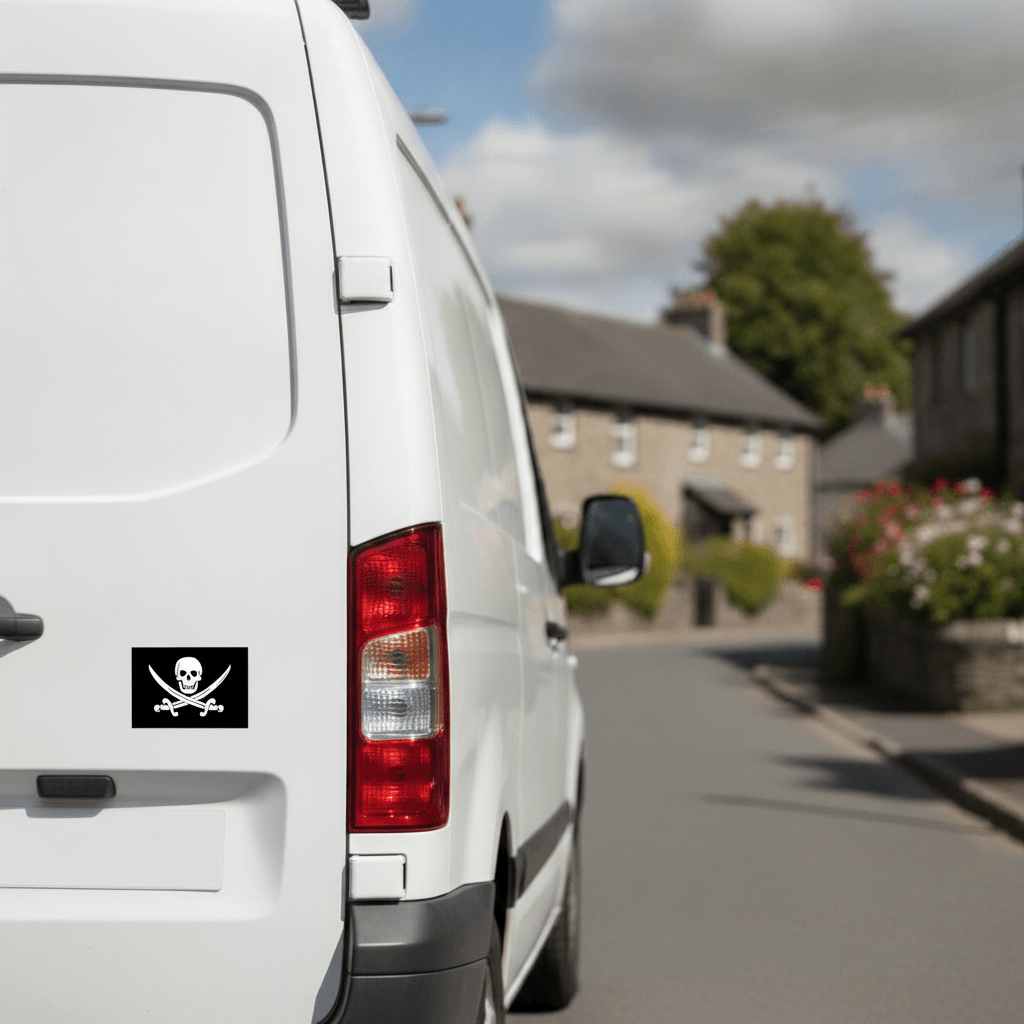 White van with a jolly roger / pirate flag sticker on the back, driving down a street.