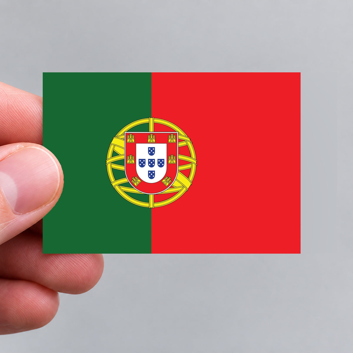 A small rectangular Portugal flag sticker held between fingers against a plain light gray background