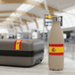 Beige water bottle with Spanish flag design next to a suitcase in an airport setting