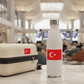 White water bottle with Turkish flag sticker next to a beige suitcase in an airport terminal.