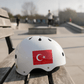 White kids skate helmet with Turkish flag sticker on a wooden bench at a skatepark