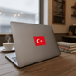 Laptop with a Turkish flag sticker on a wooden desk with a cup of coffee and books in the background.