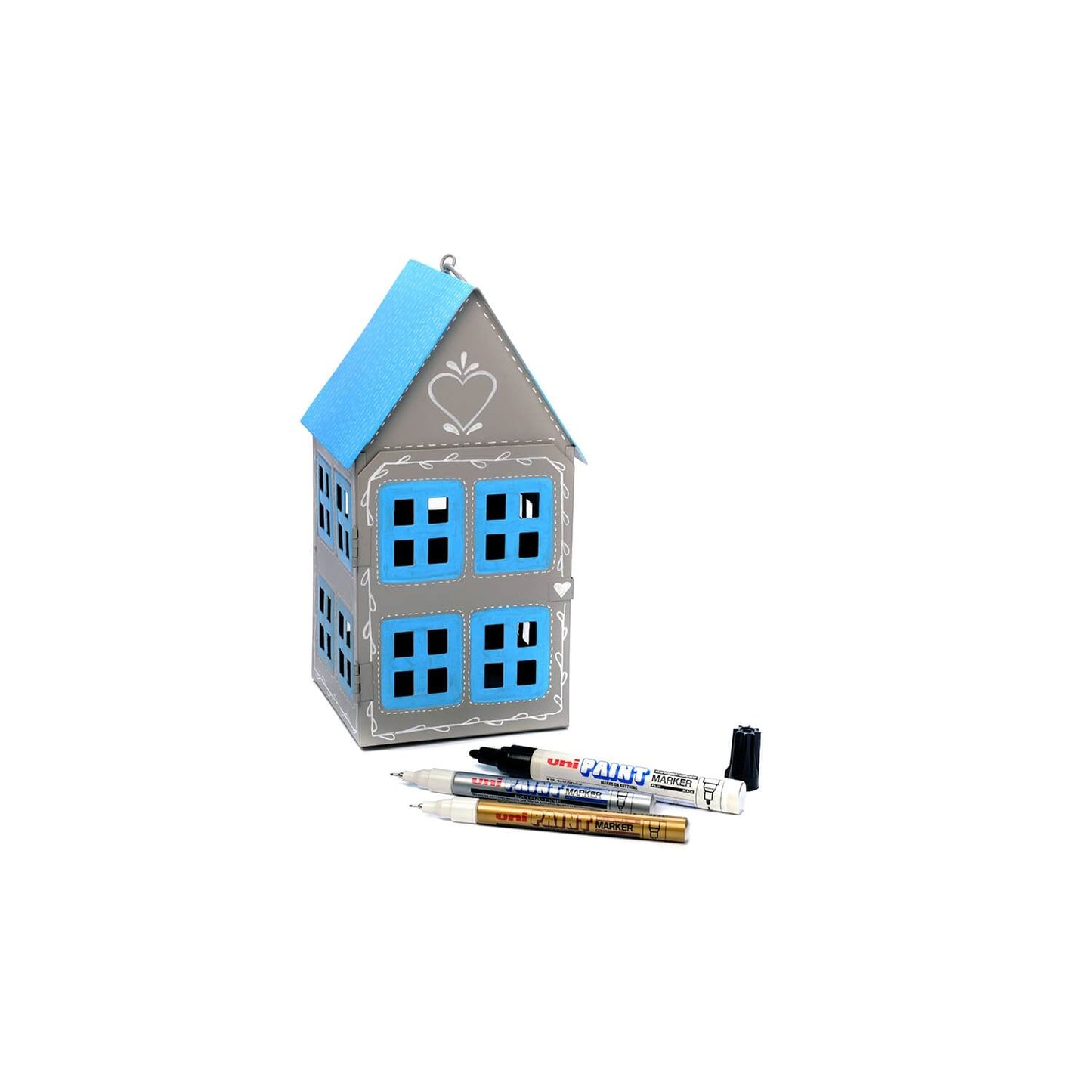 Painted cardboard house with blue accents and three pens on a white background