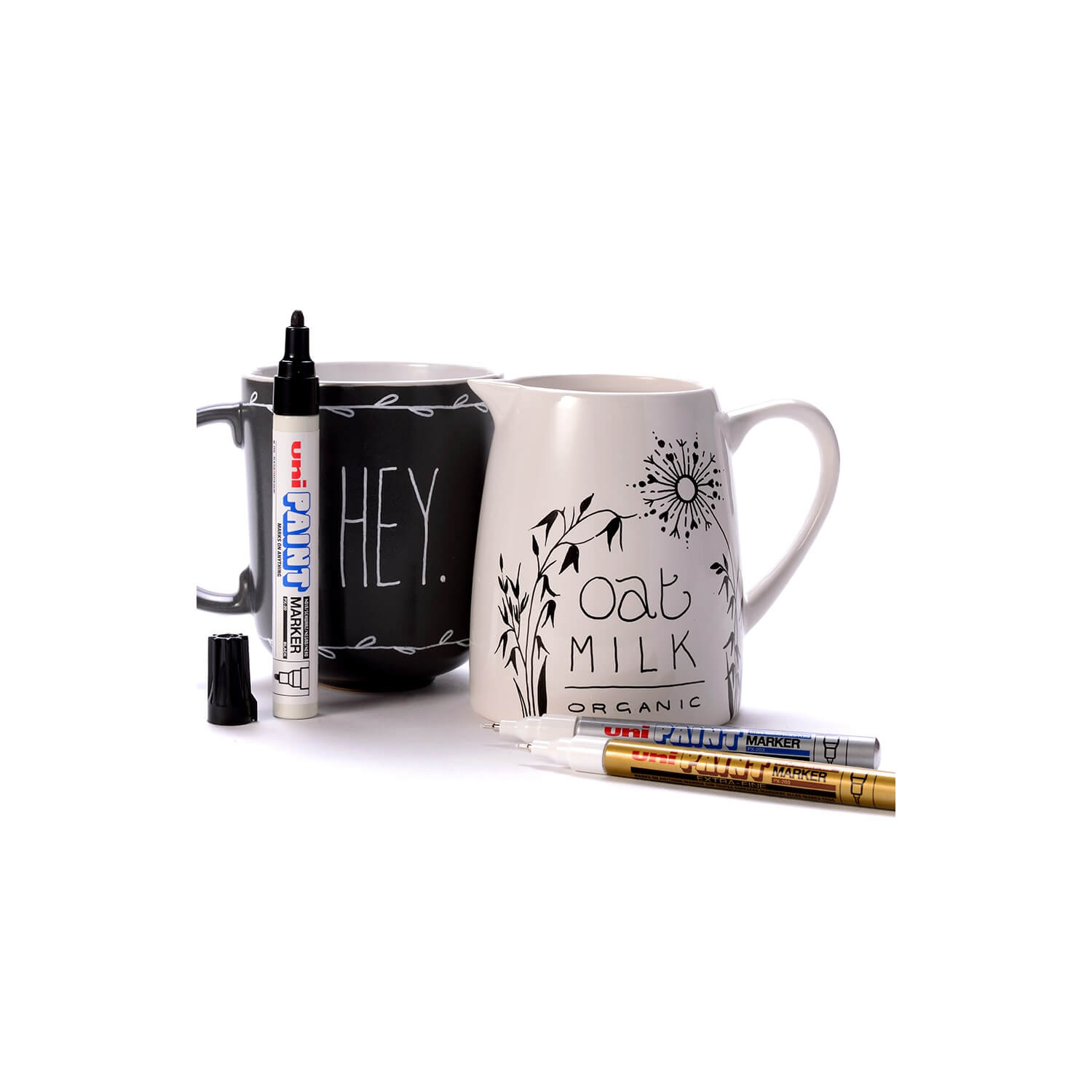 Mug with 'Oat Milk Organic' text, black mug with 'HEY' text, and markers on a white background